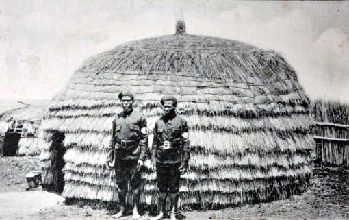 A group of men standing in front of a straw hut AI-generated content may be incorrect.